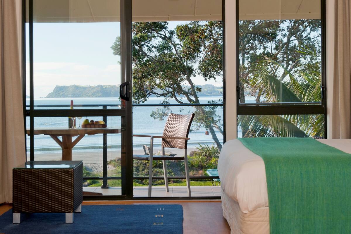 Ein Schlafzimmer mit großem Fenster, Blick auf Strand und Bäume.