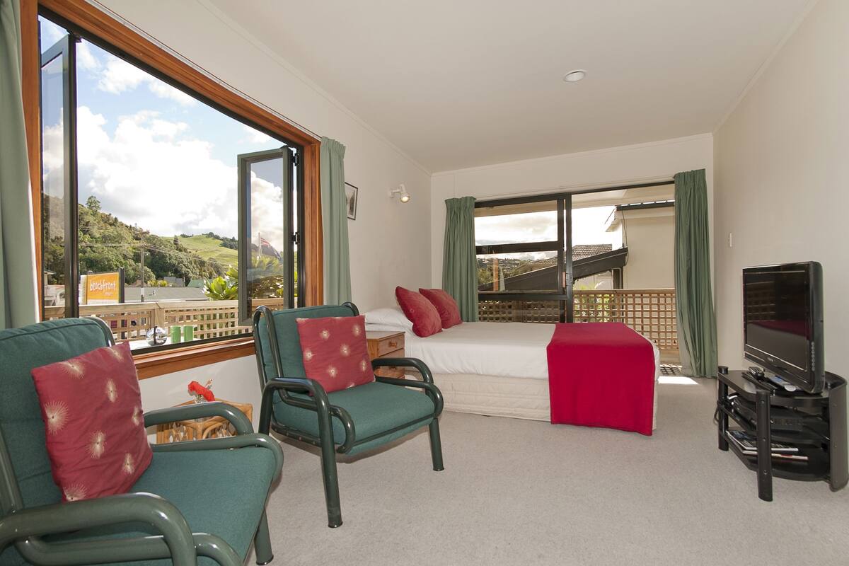 Ein Hotelzimmer mit Bett, Fernseher, Balkon und zwei Sesseln.