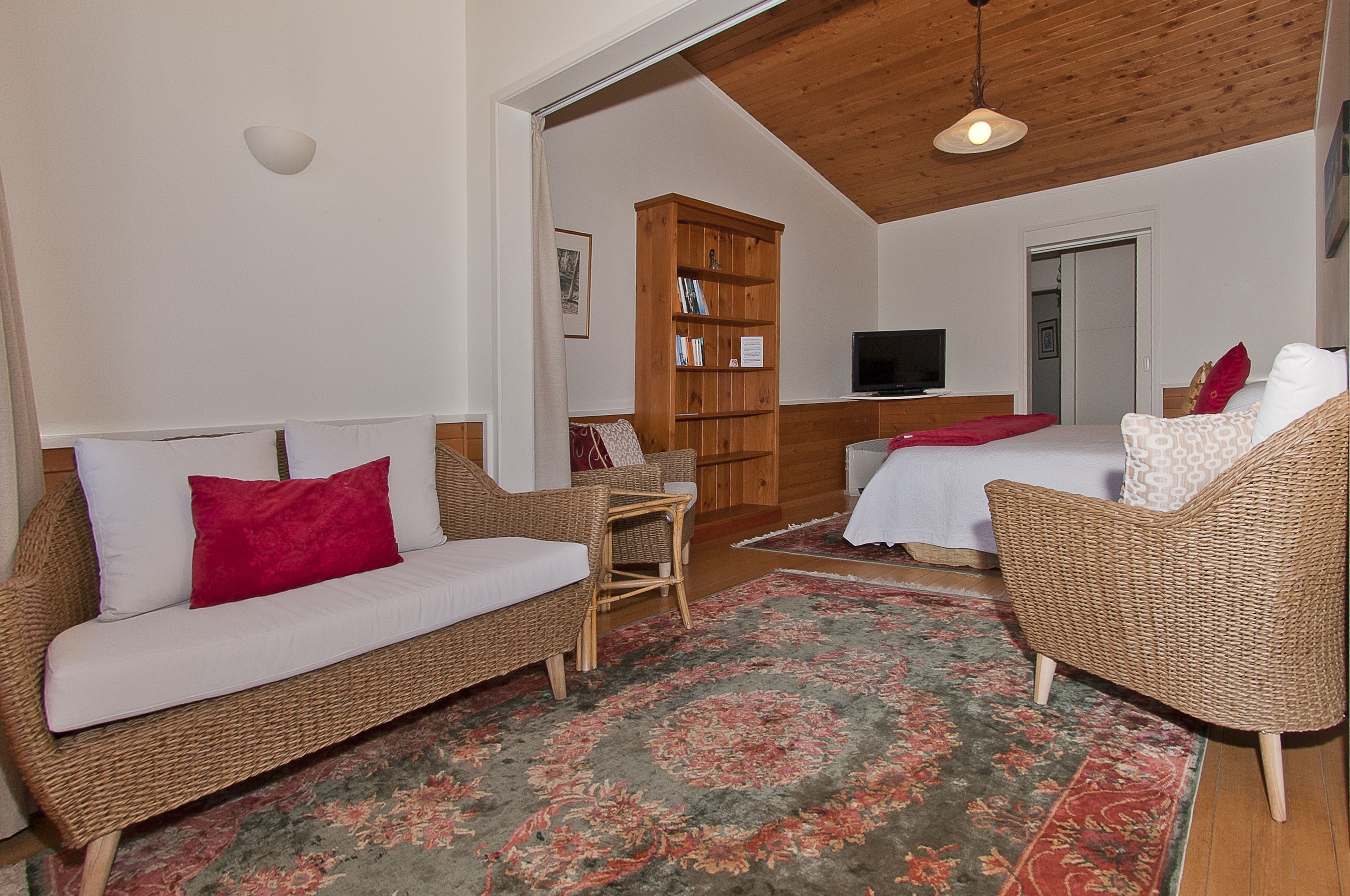 Un salón acogedor con muebles de mimbre, una estantería, un televisor y una cama.