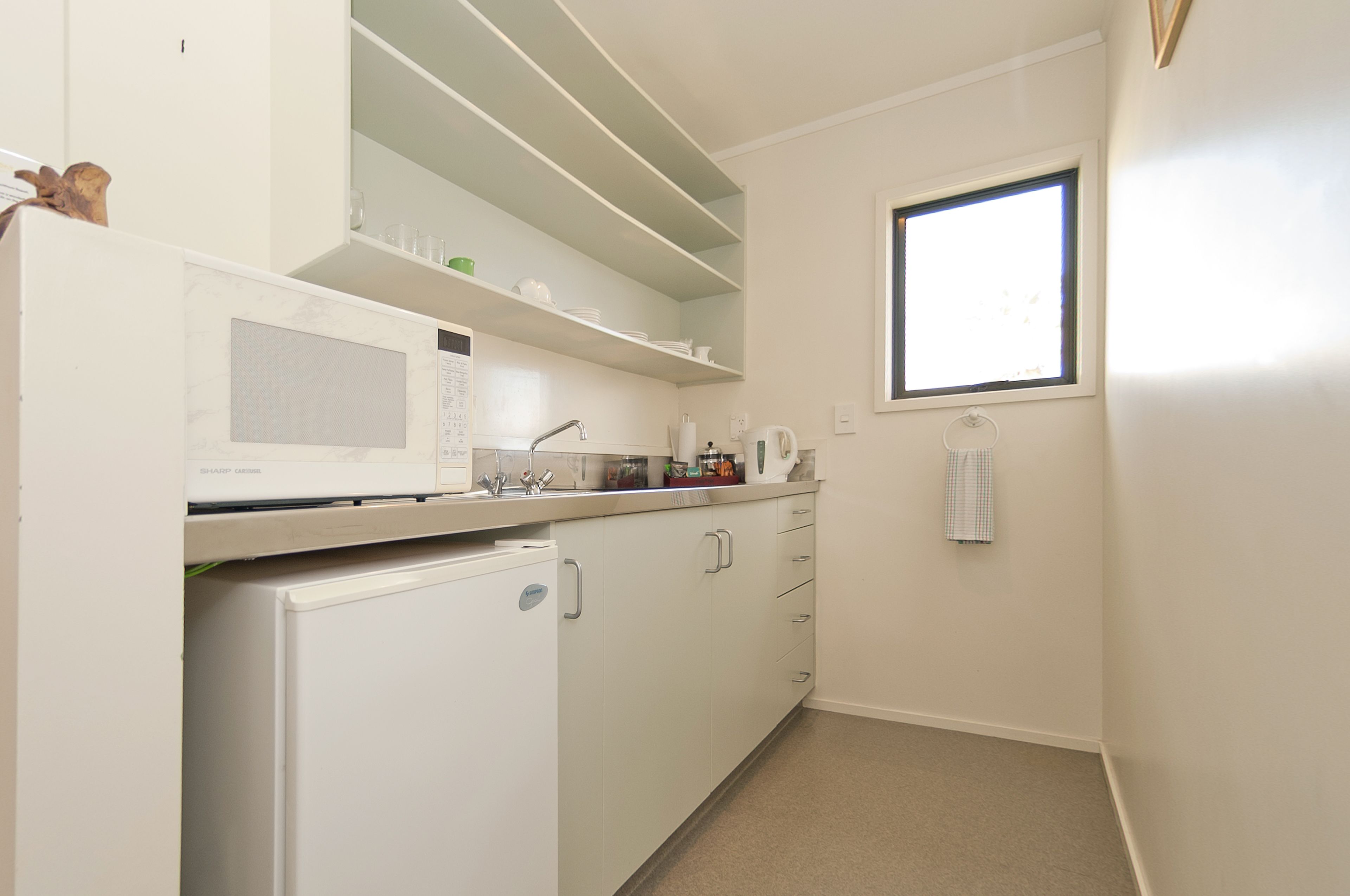 Cocina compacta con electrodomésticos blancos, una ventana y una toalla colgada en la pared.