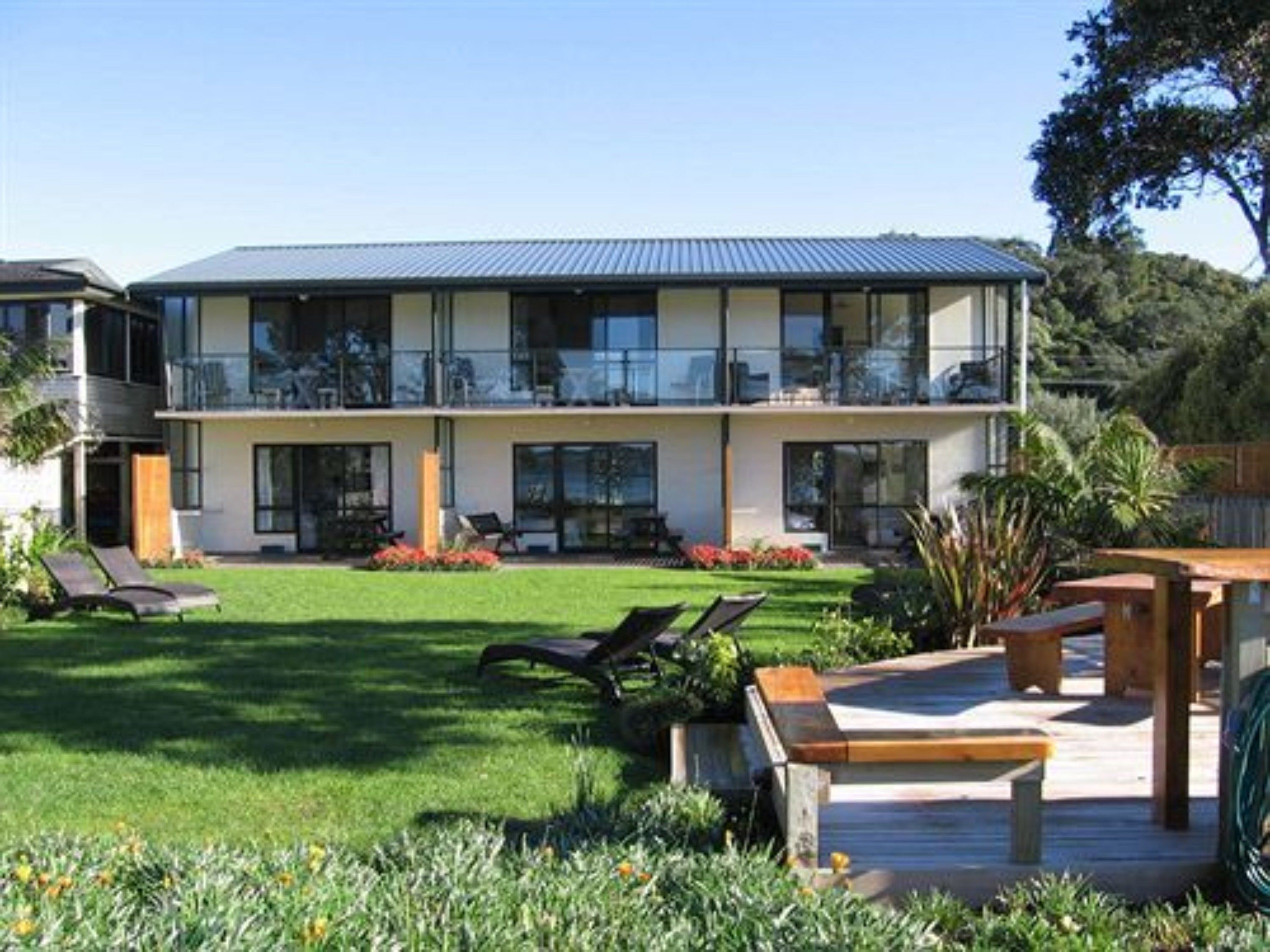 A modern two-story house with a large balcony, a well-maintained lawn, and outdoor seating.