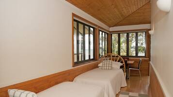 A room with two single beds, a wooden ceiling, large windows, and a checkered rug.