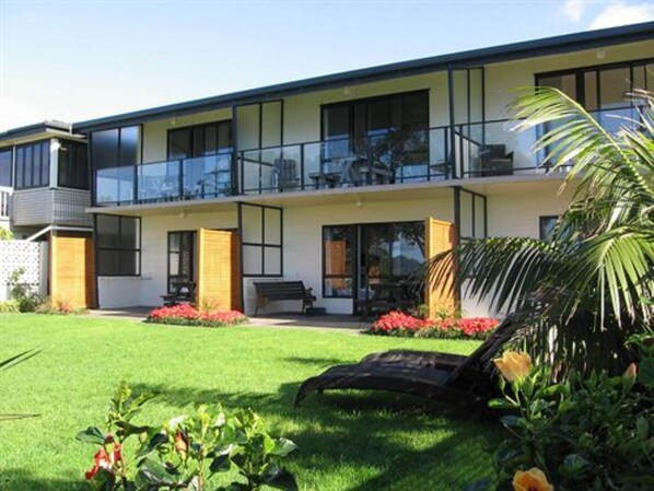 A modern two-story house with a balcony, a well-maintained lawn, and a garden with red flowers.