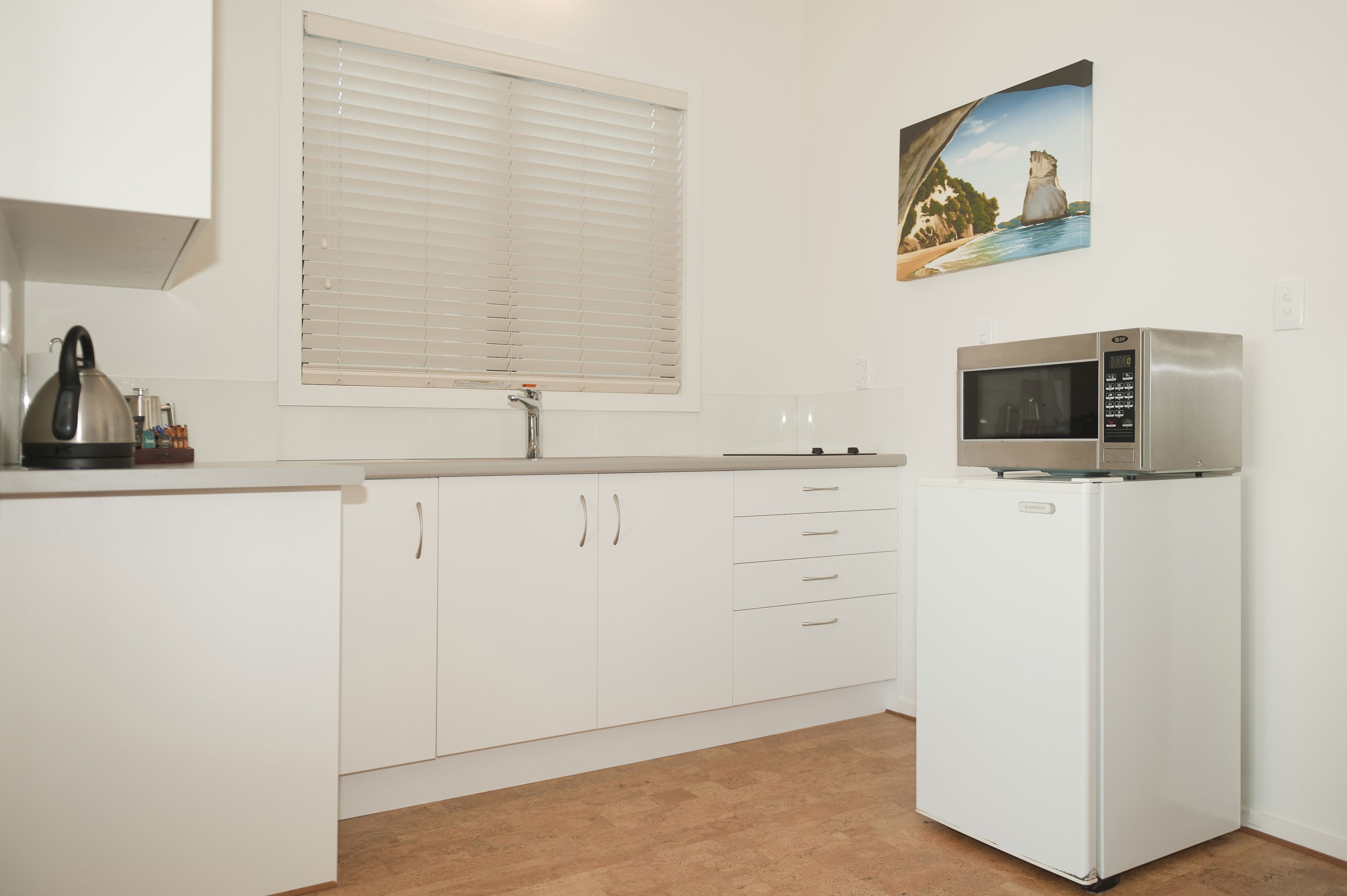 A kitchen with white cabinets, a stainless steel microwave, and a kettle on the counter.