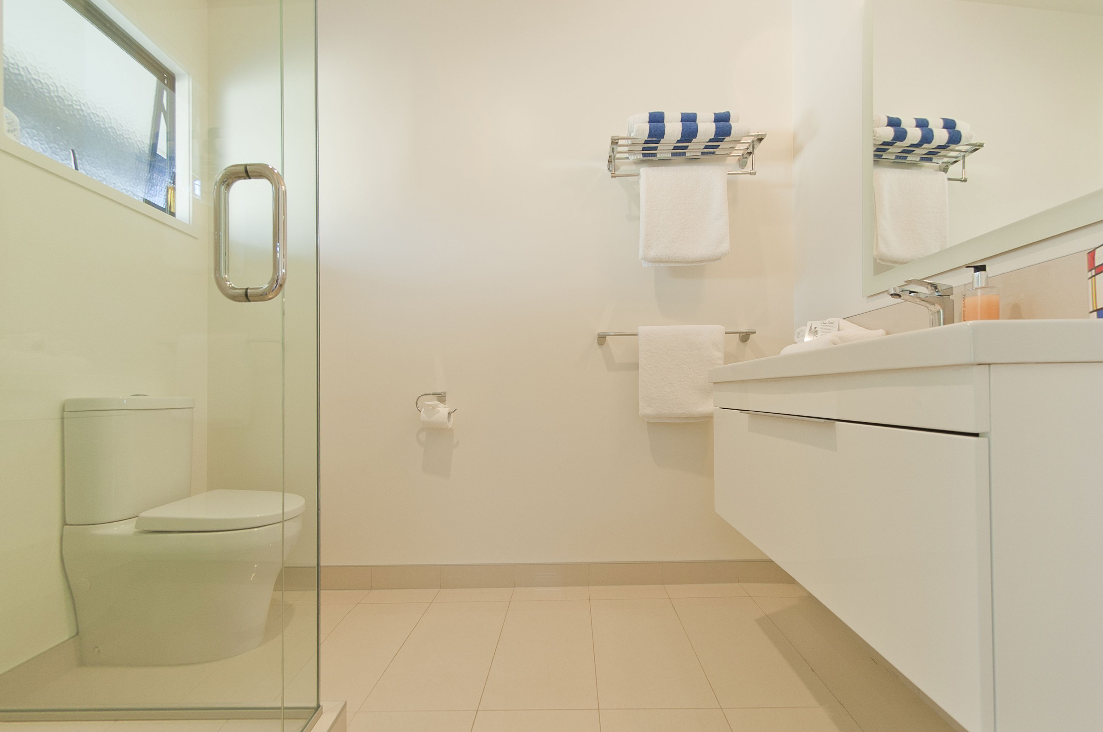 A modern bathroom with a glass shower enclosure, a toilet, a sink with a mirror, and two towel racks with striped towels.
