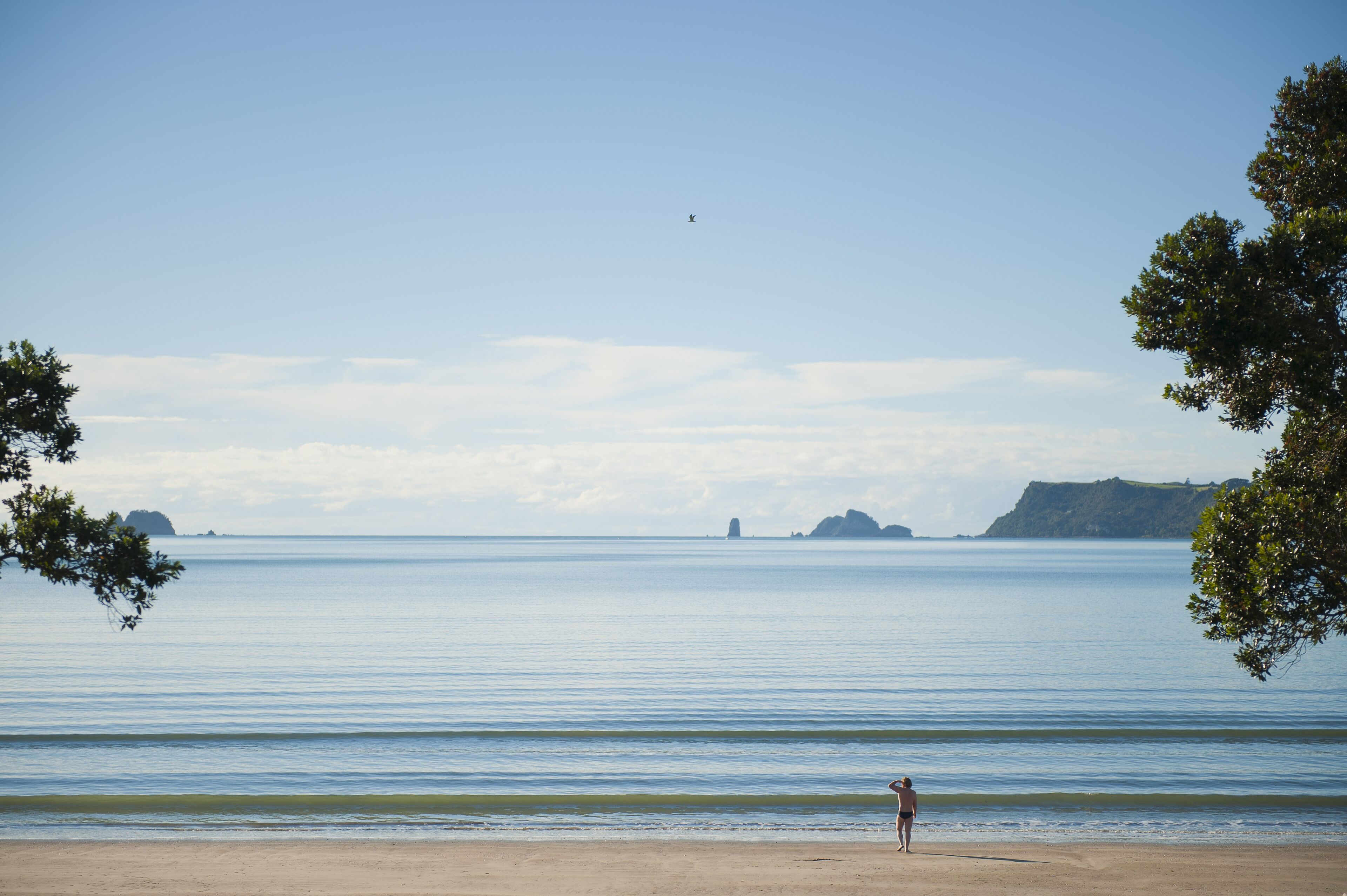 A beach with calm water, distant landforms, and a person standing on the shore.