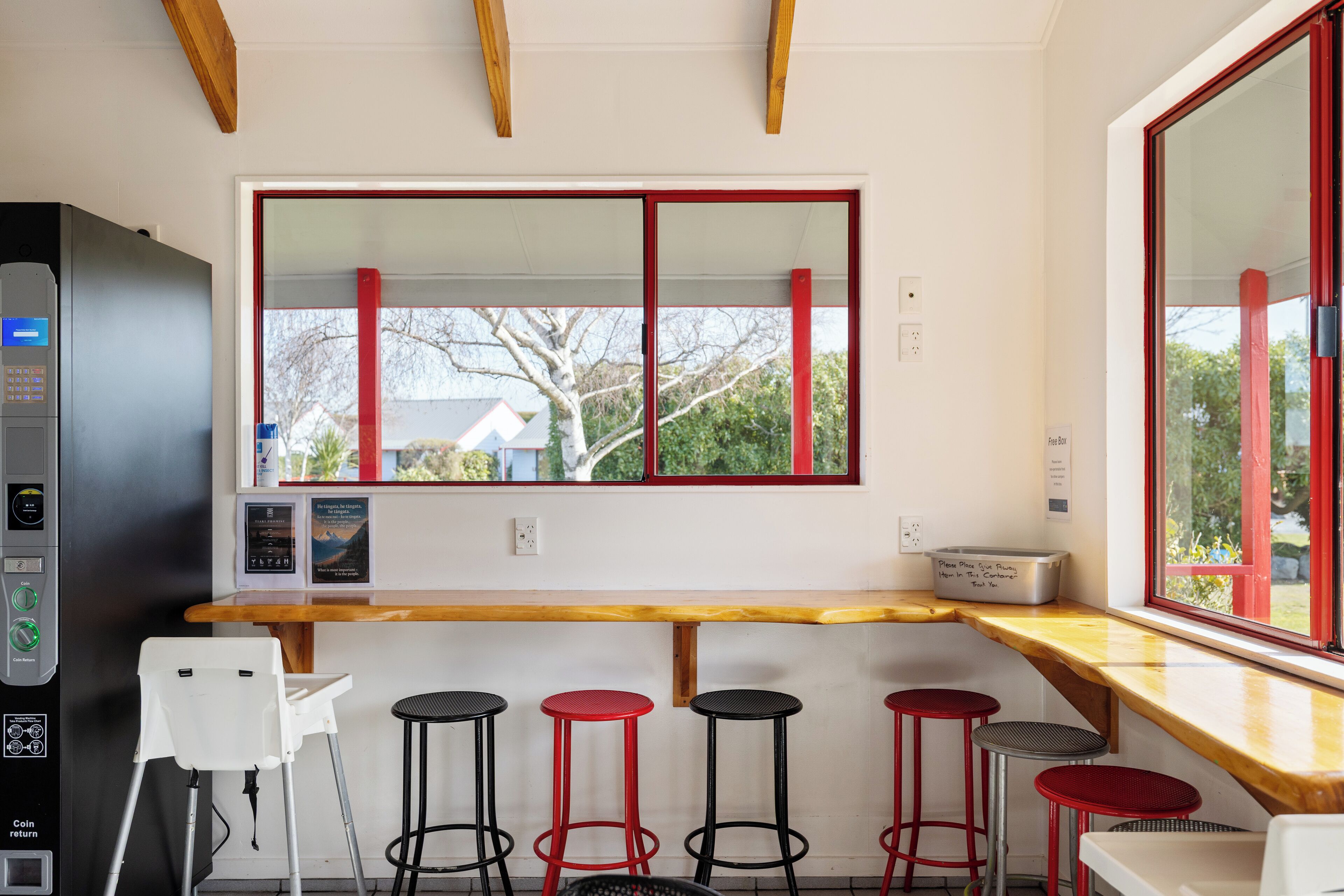 A modern kitchen with a wooden countertop, a large window with red frames, and four stools.