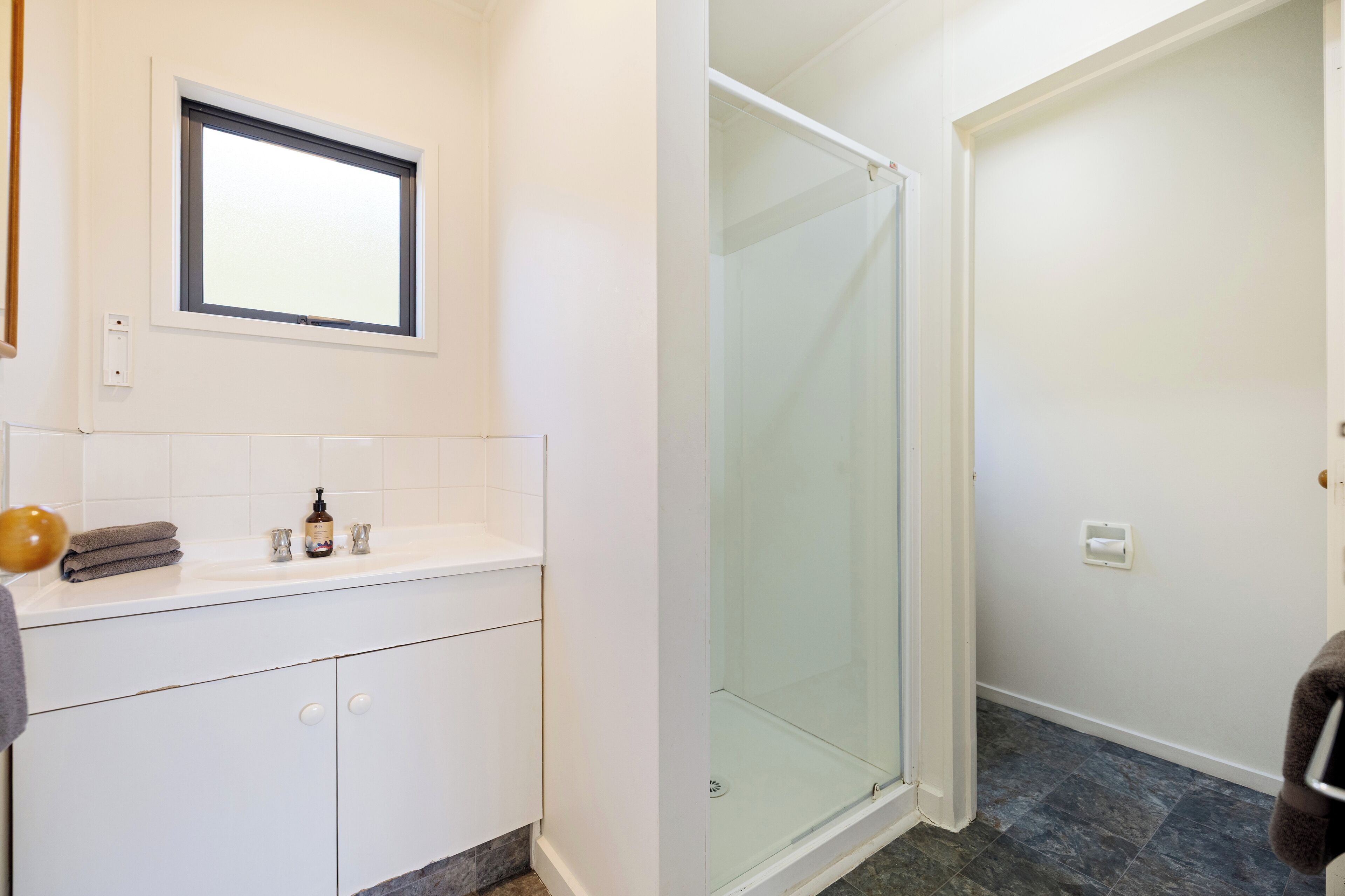 A bathroom with a white vanity, a glass shower enclosure, and a window above the sink.