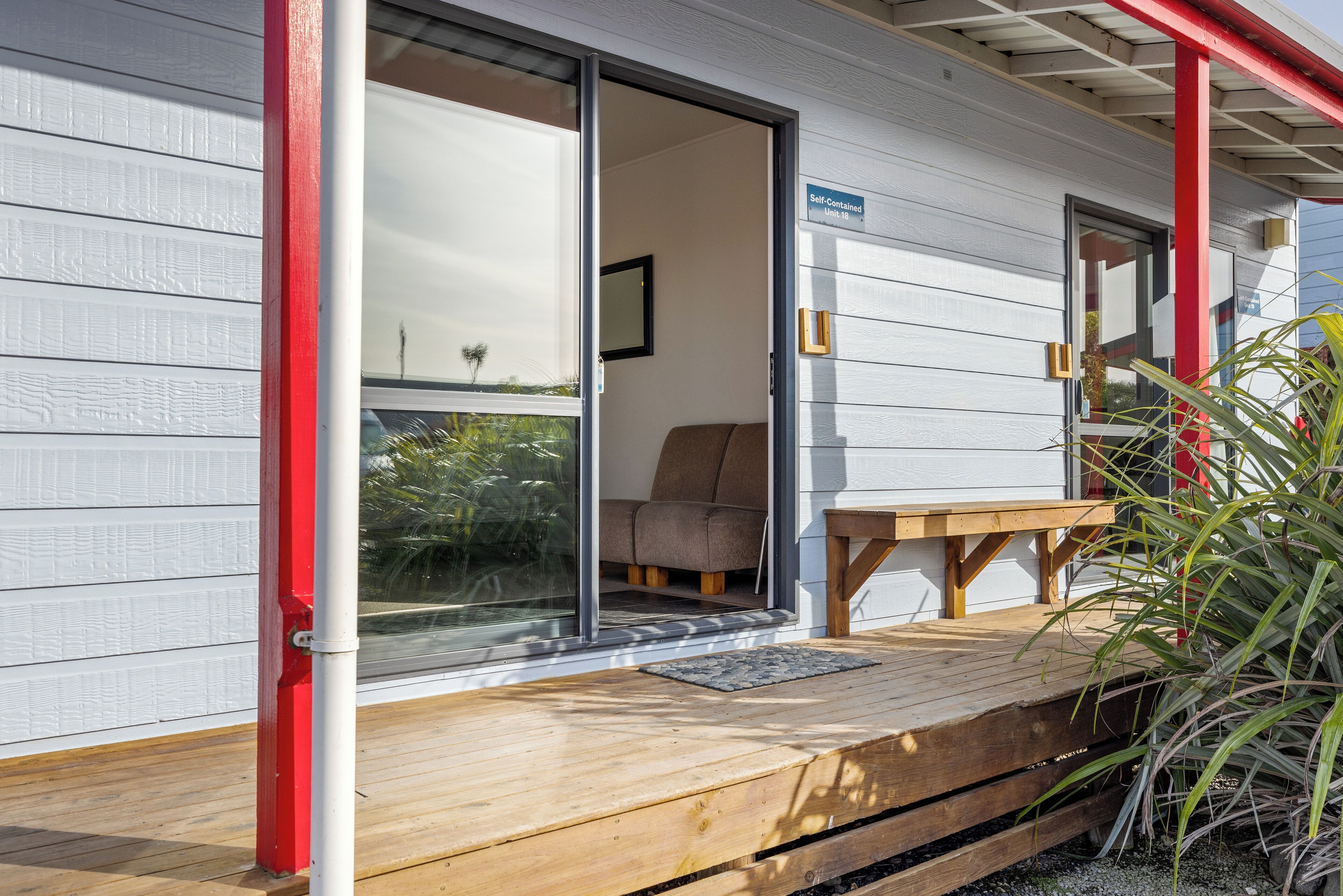 A wooden deck with a bench and a table, a sliding glass door, and a sign indicating 'Self-Contained Unit 18'.