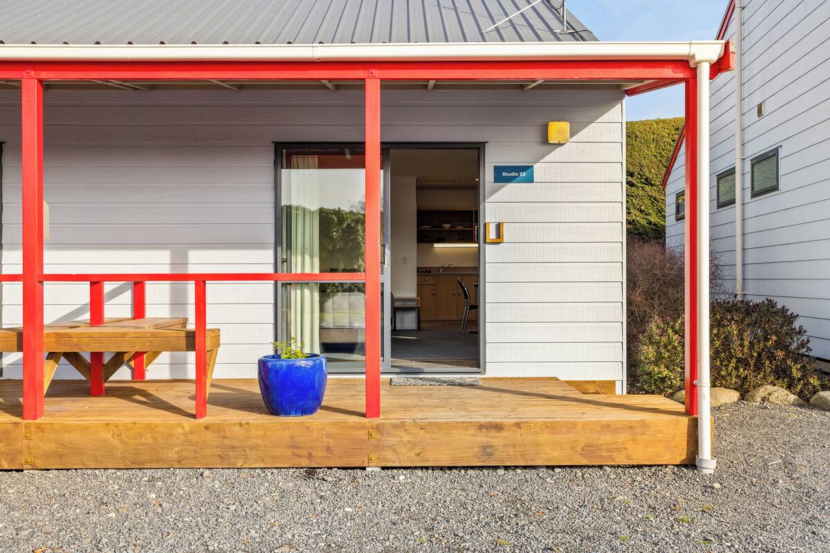 Un bâtiment doté d’une entrée abritée, d’un banc en bois et d’un grand bac à fleurs bleu.