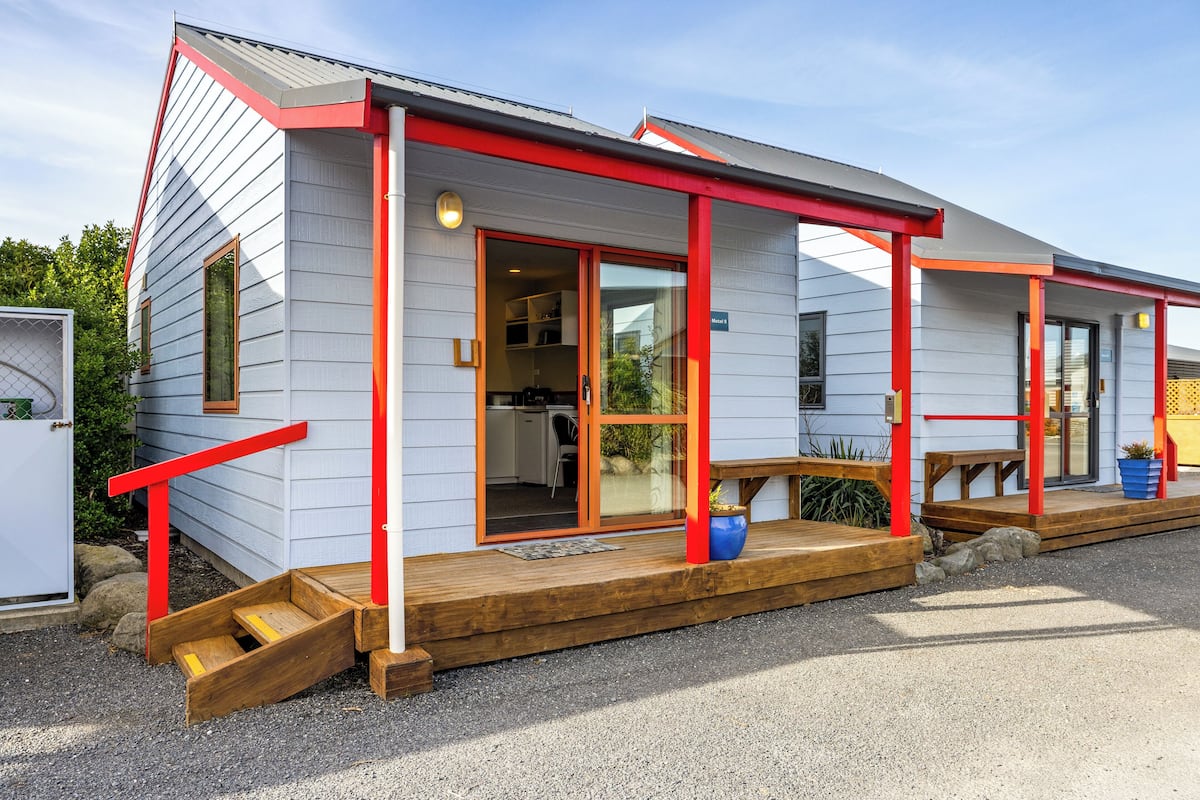 Une maison moderne dotée d’une terrasse en bois, d’une rambarde rouge et d’une grande porte-fenêtre coulissante.
