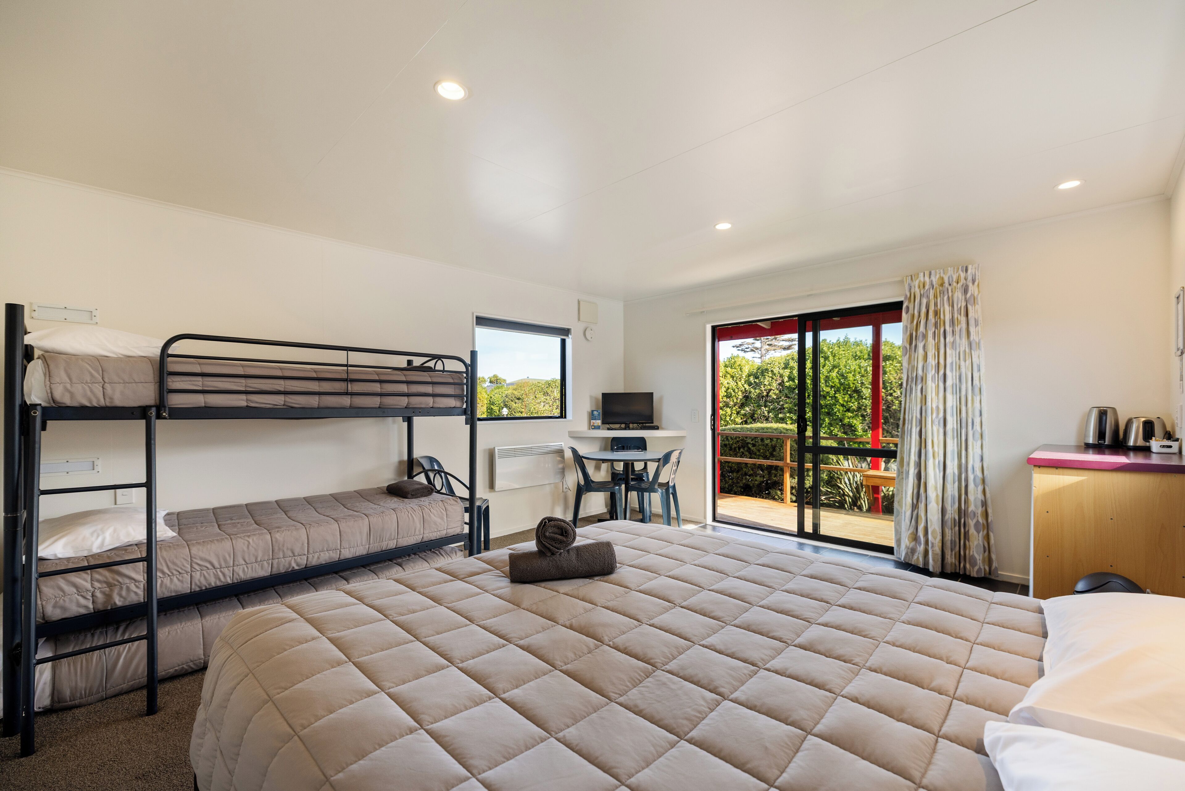 A hotel room with bunk beds, a desk with a computer, a chair, and a view of the outdoors.
