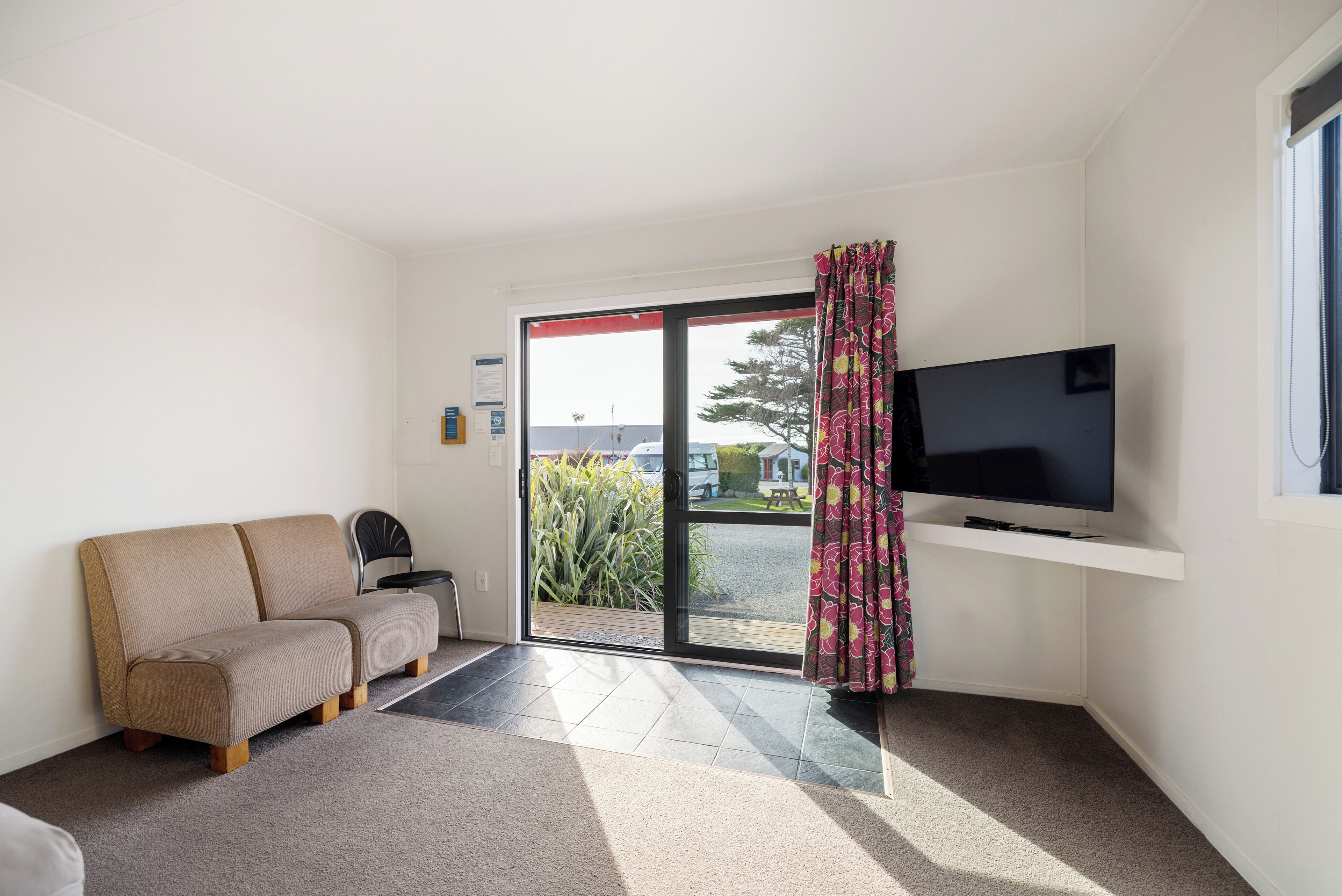 Una habitación con sofá, televisor sobre un mueble bajo y puerta corrediza de vidrio que da a un espacio exterior.