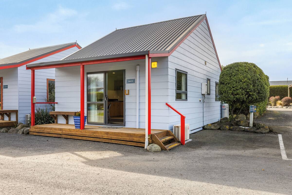 Un petit bâtiment d’un seul étage, doté d’une entrée encadrée de rouge et d’une terrasse en bois.
