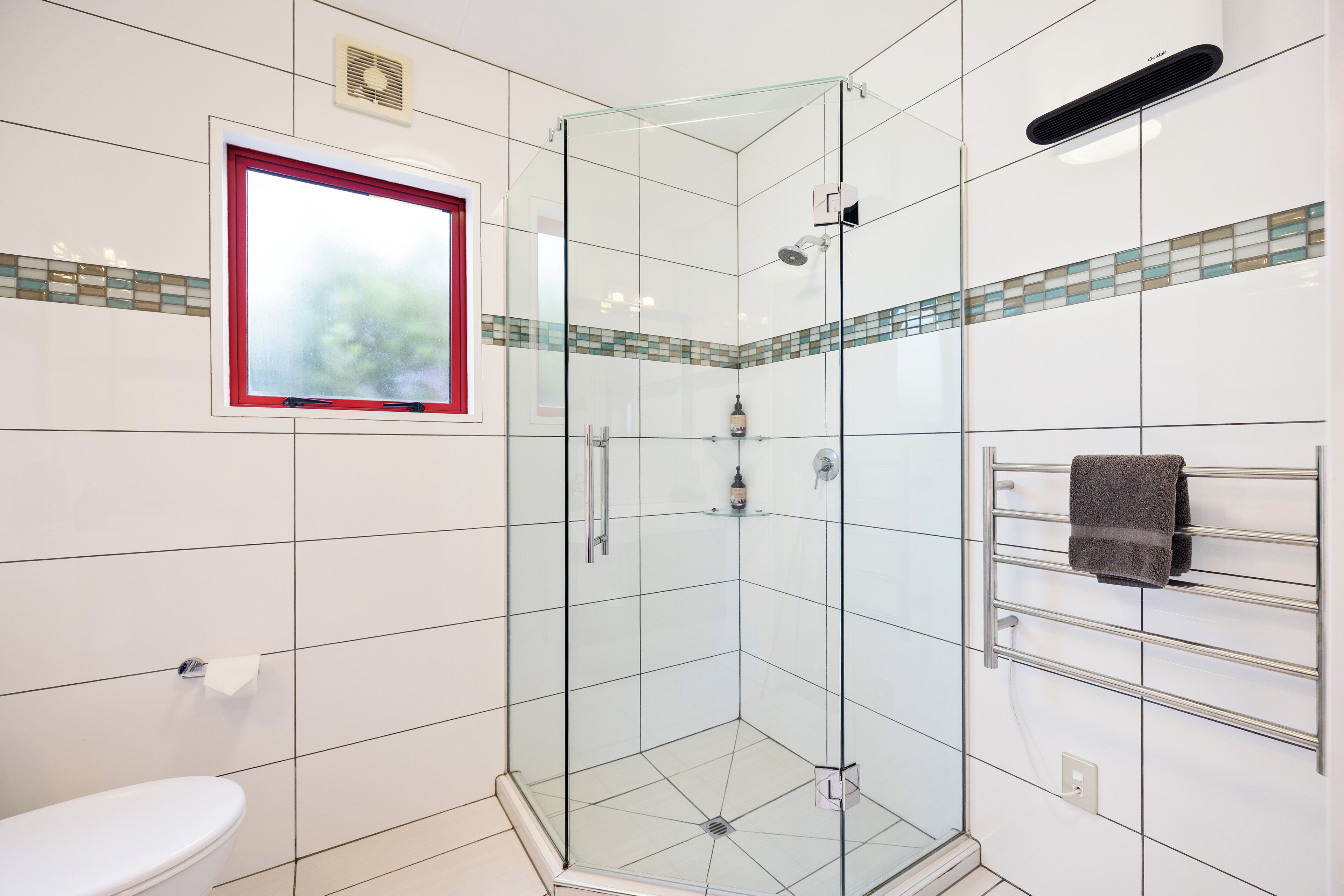 A modern bathroom with a glass-enclosed shower, a toilet, and a towel rack.