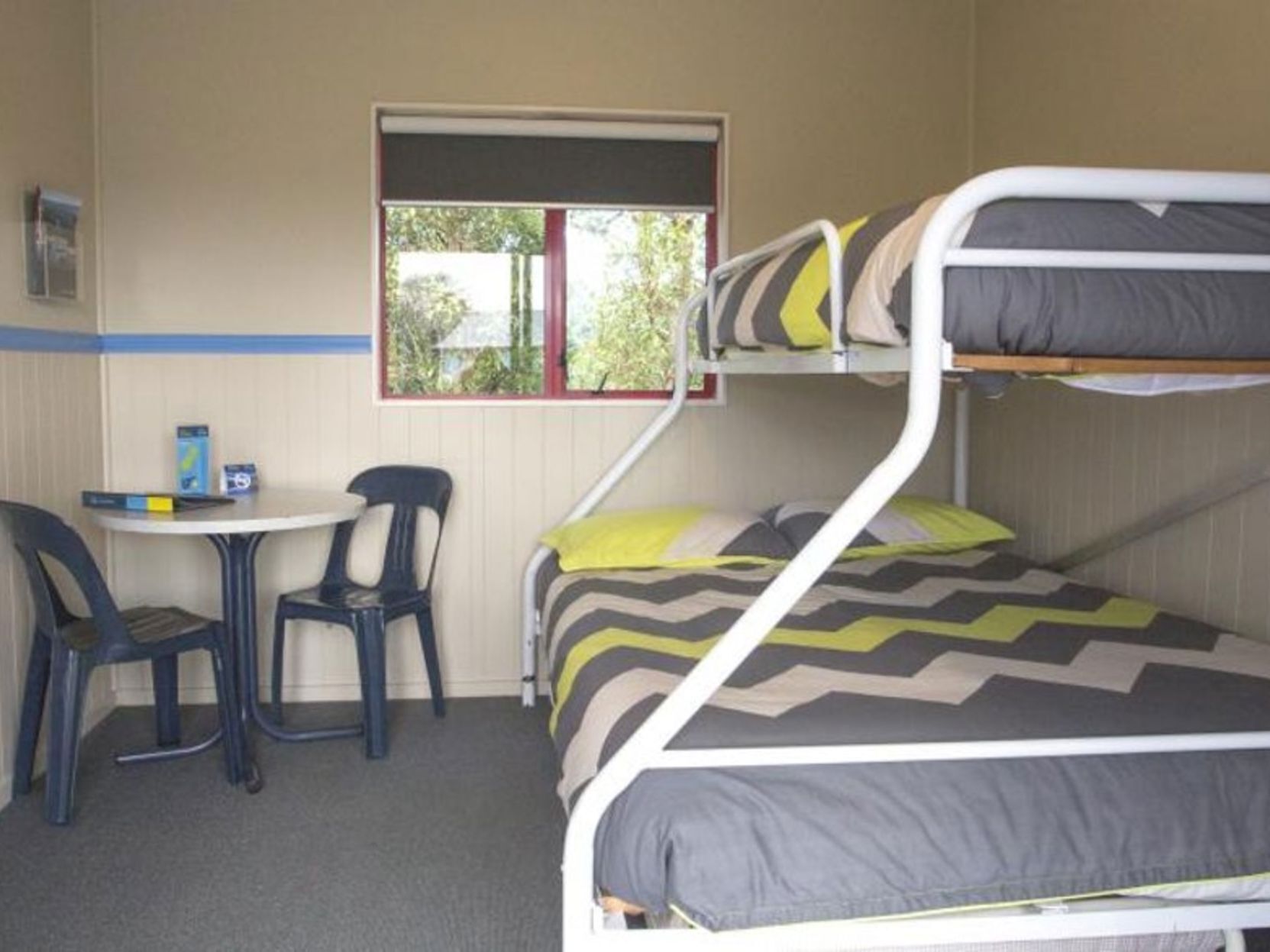 Un lit superposé avec un bureau et deux chaises, une fenêtre donnant sur un paysage verdoyant et une étagère murale avec quelques objets.