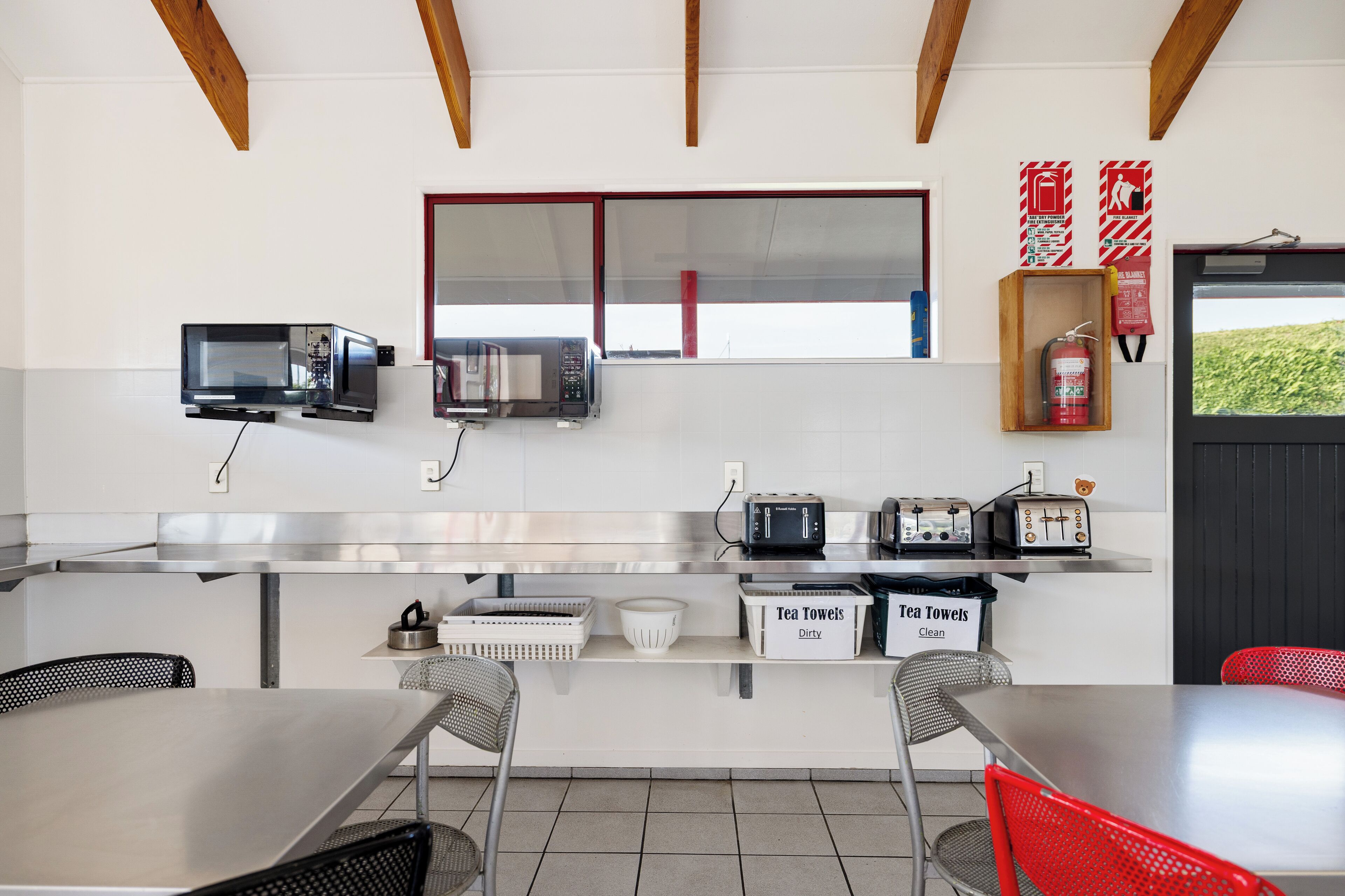 A kitchenette with two microwaves, a toaster, and a fire extinguisher. There are two baskets labeled 'Tea Towels Dirty' and 'Tea Towels Clean'.