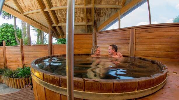 Een houten jacuzzi met metalen frame, omgeven door houten wanden en een houten terras.