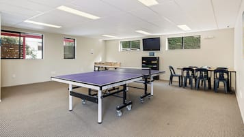 Una habitación con dos mesas de ping pong, un televisor y una ventana con vistas a árboles.