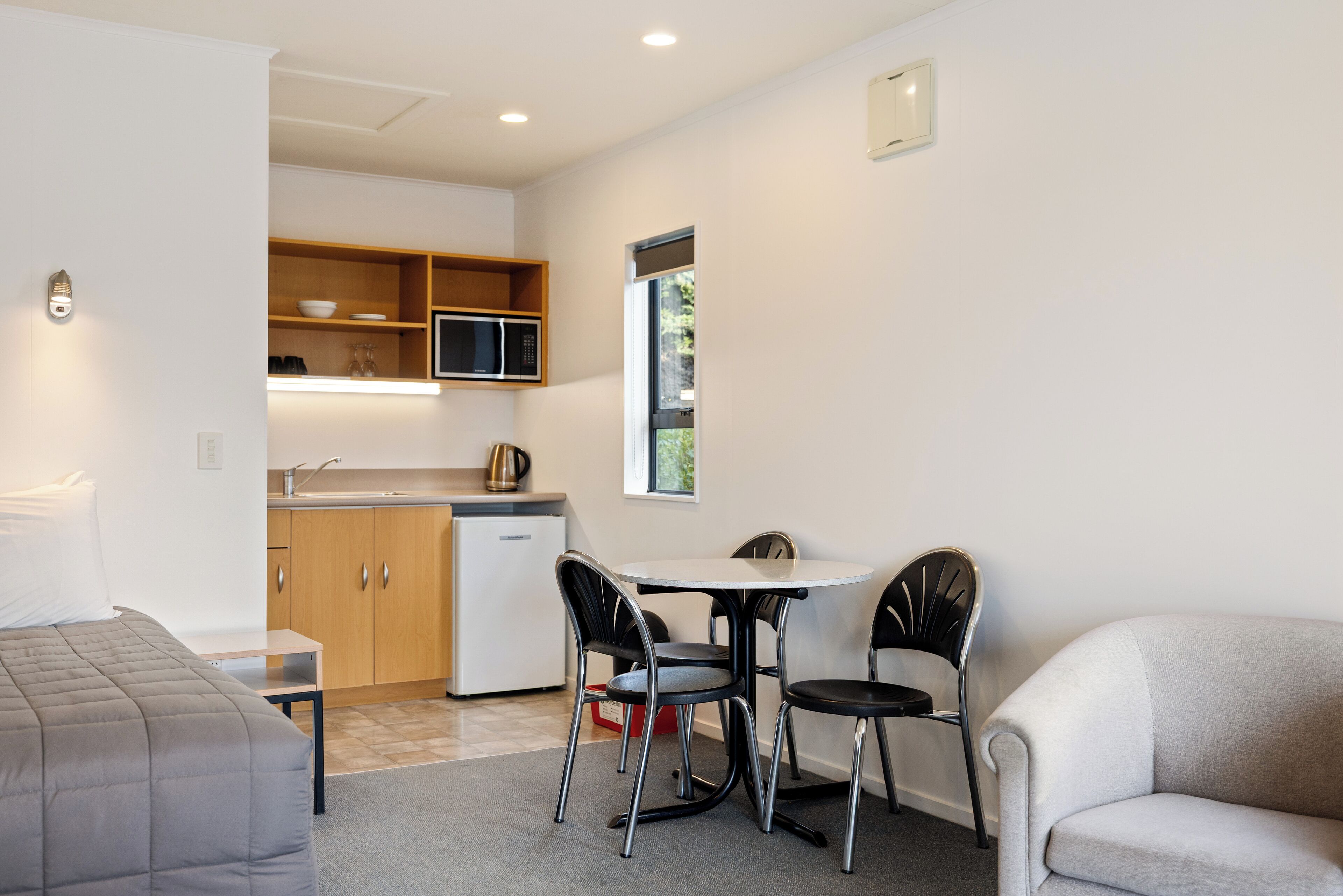 A compact hotel room with a kitchenette, a dining area with a table and chairs, a sofa, and a bed.