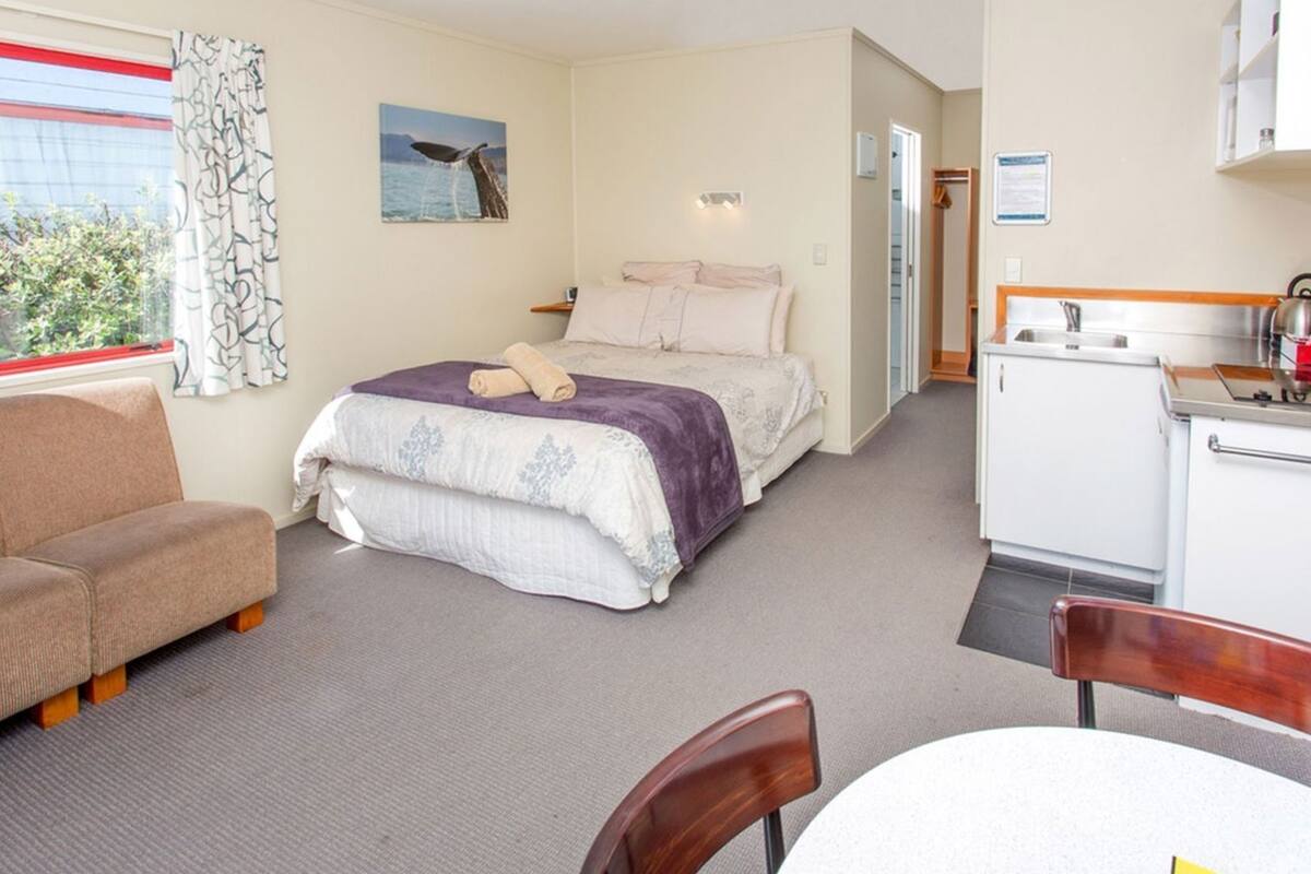 Une chambre d’hôtel équipée d’un lit, d’un bureau, d’une chaise, d’une petite kitchenette et d’une fenêtre avec des rideaux.