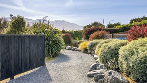 Een grindpad dat door een aangelegde tuin slingert, met diverse struiken en een houten omheining.