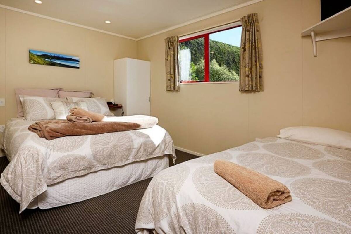 Une chambre d’hôtel avec un lit, une armoire, une fenêtre avec des rideaux et un tableau au mur.