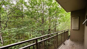 Een balkon met een metalen hekwerk, met uitzicht op een dicht bos.
