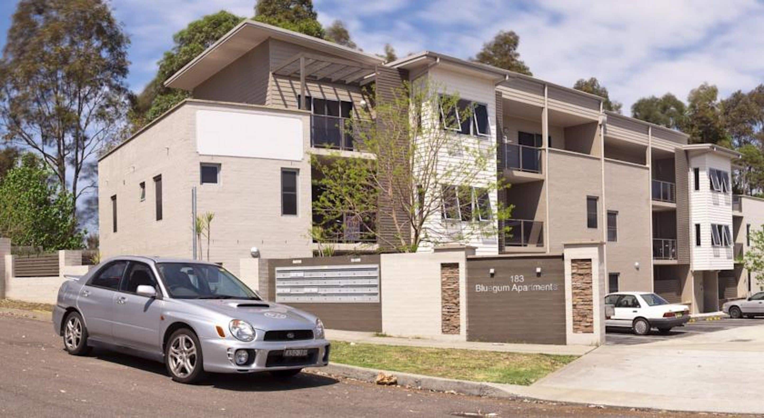 Un immeuble d’appartements à plusieurs étages avec une entrée de garage, une voiture garée devant et un ciel dégagé.