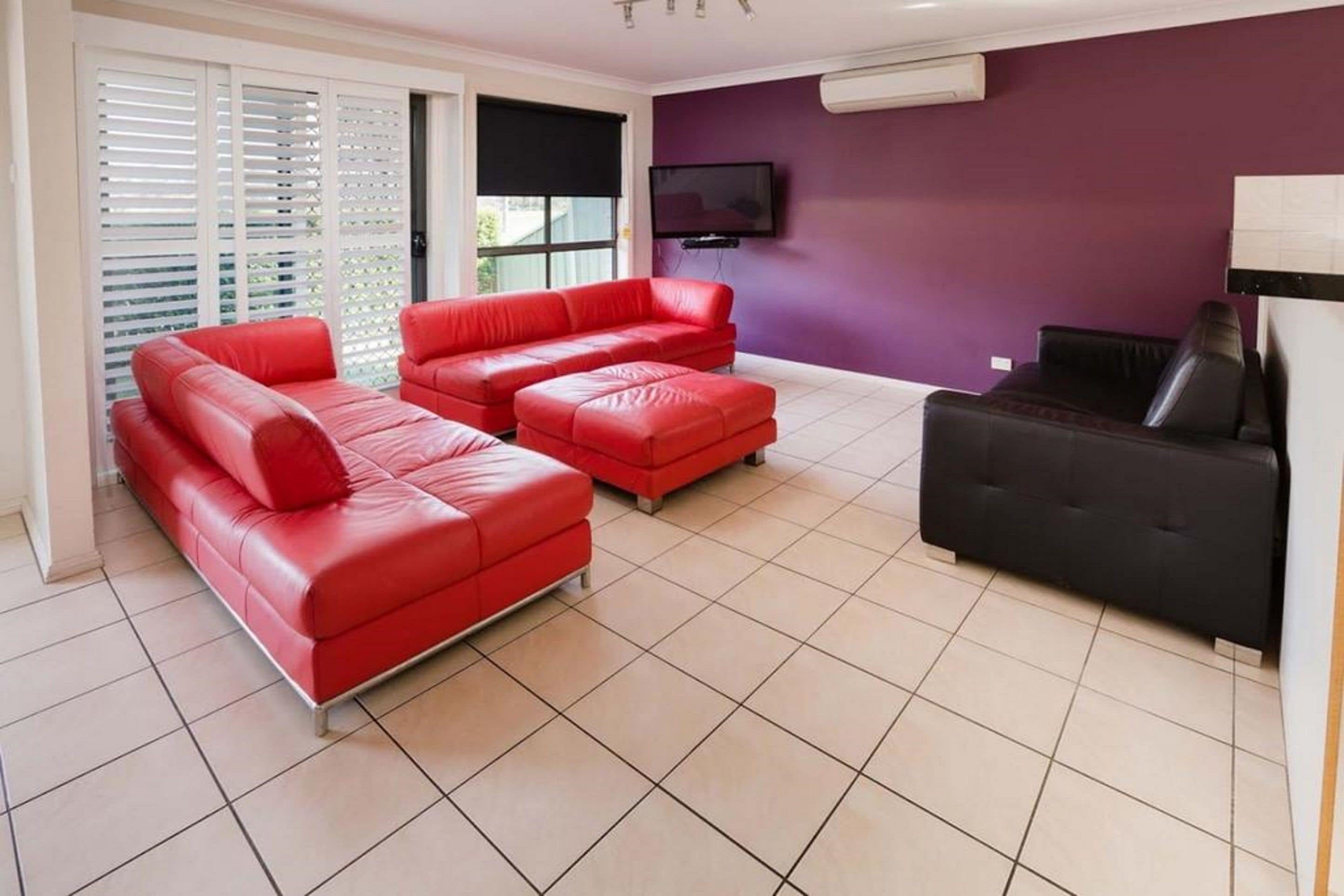A living room with two red leather sofas, a black sofa, and a flat-screen TV mounted on the wall.