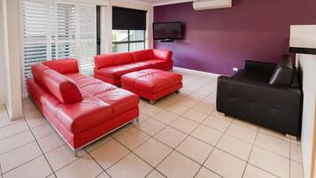 A living room with two red leather sofas, a black sofa, and a flat-screen TV mounted on the wall.