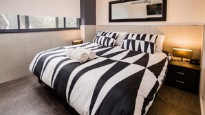 Een hotelkamer met een groot bed, zwart-wit gestreepte beddengoed, een bedlampje en een nachtkastje met een klok.