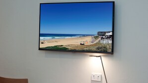 Televisor de pantalla plana montado en una pared mostrando una playa con cielo azul despejado y océano.