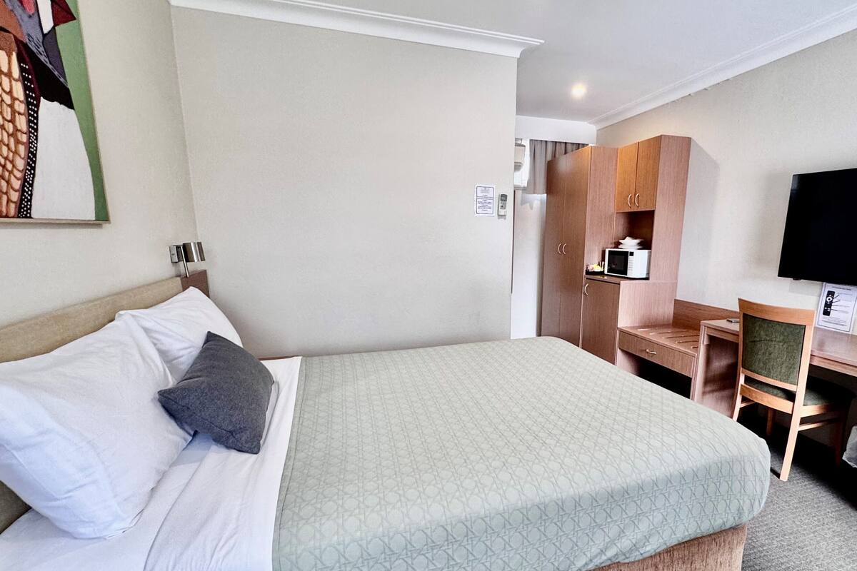A hotel room with a bed, a desk with a chair, a television, and a microwave.