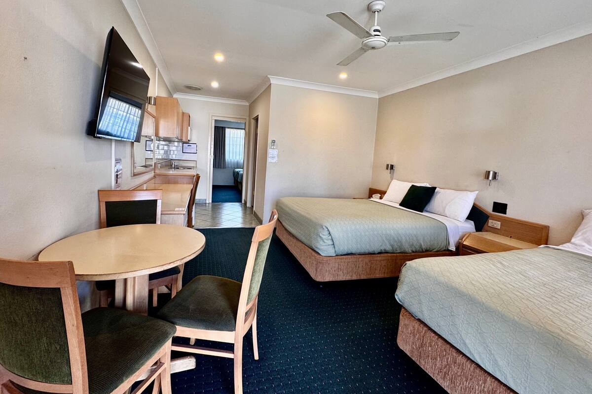 A hotel room with two beds, a desk with a chair, a television, and a ceiling fan.