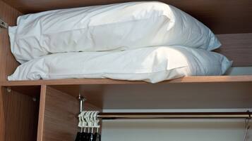 Un armario de madera con barra para colgar y estante con ropa de cama blanca doblada con cuidado.