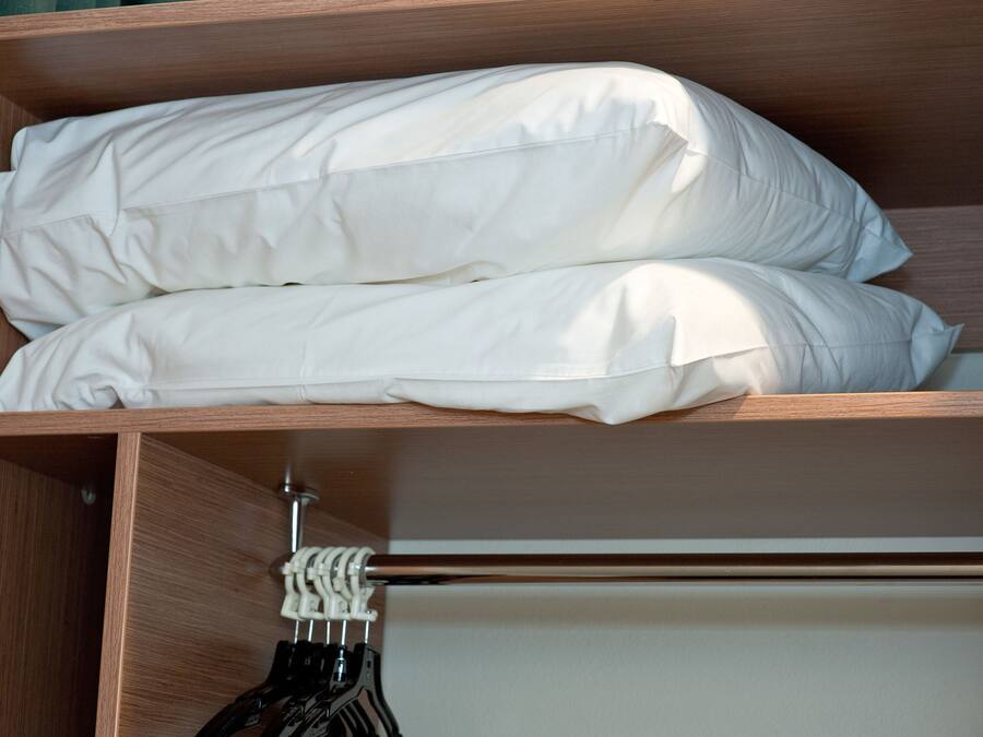 Une armoire en bois, dotée d’une tringle pour suspendre les vêtements et d’une étagère où sont soigneusement pliés des draps blancs.