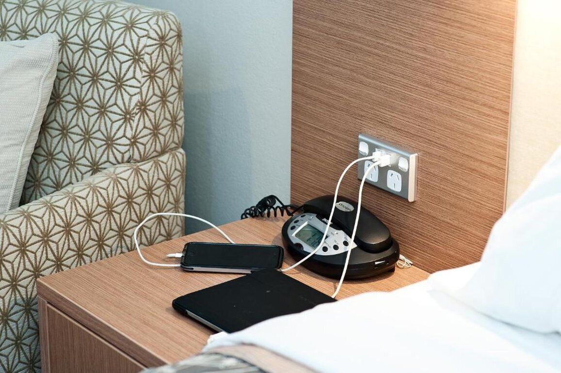 Un lit bien fait, avec un oreiller, une table de chevet sur laquelle se trouvent un téléphone, un chargeur et une balance.