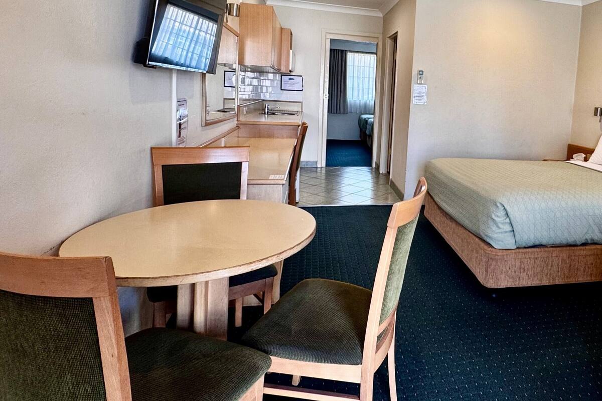 A compact hotel room with a kitchenette, a bed, a TV, and a ceiling fan.