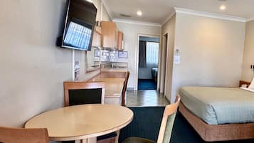 Una habitación de hotel compacta con kitchenette, una cama, un televisor y un ventilador de techo.