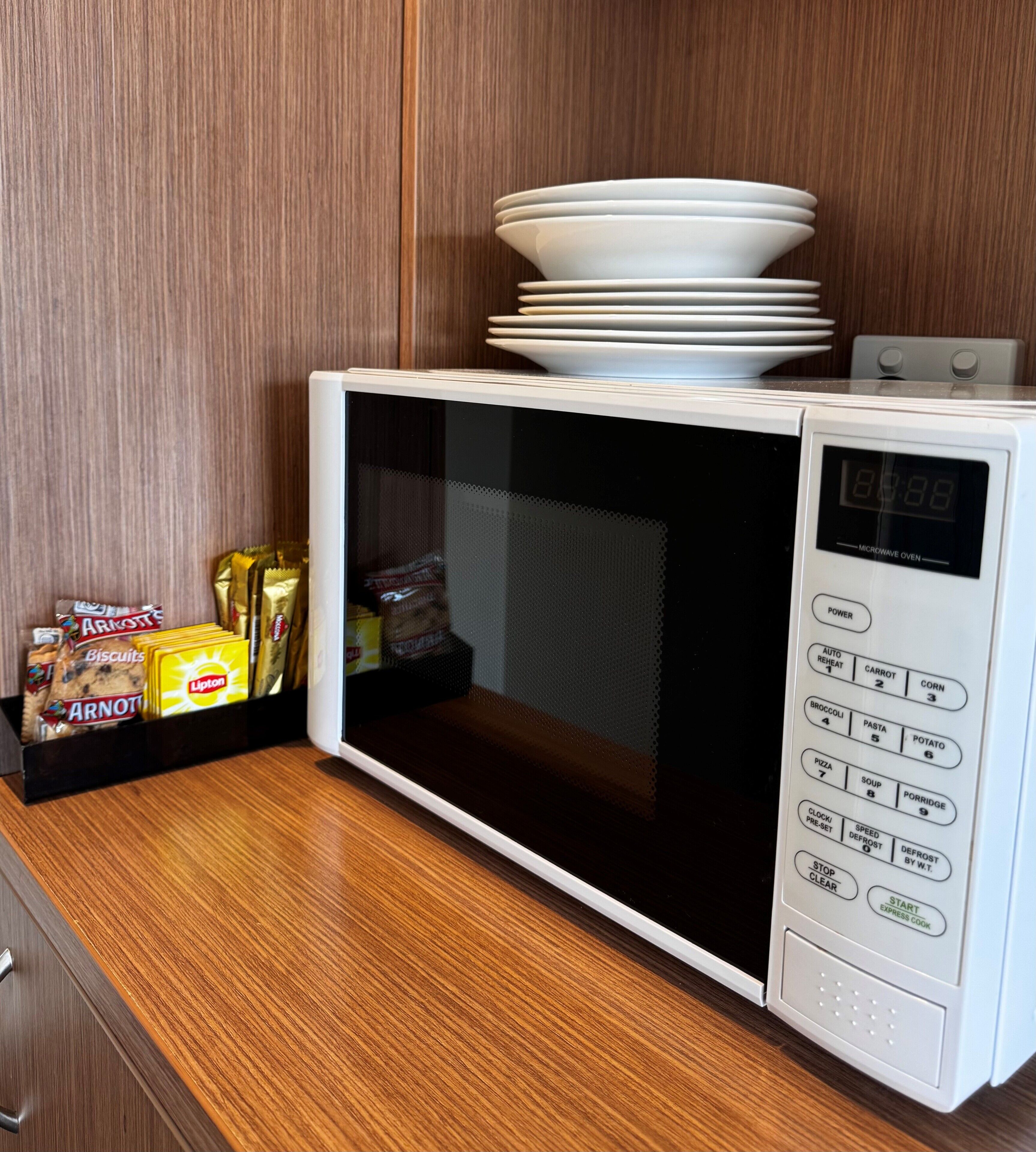 A microwave oven with a digital display, a control panel with preset options, and a stack of white plates on top.