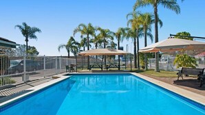 Una piscina con área cercada, palmeras y mobiliario de exterior.