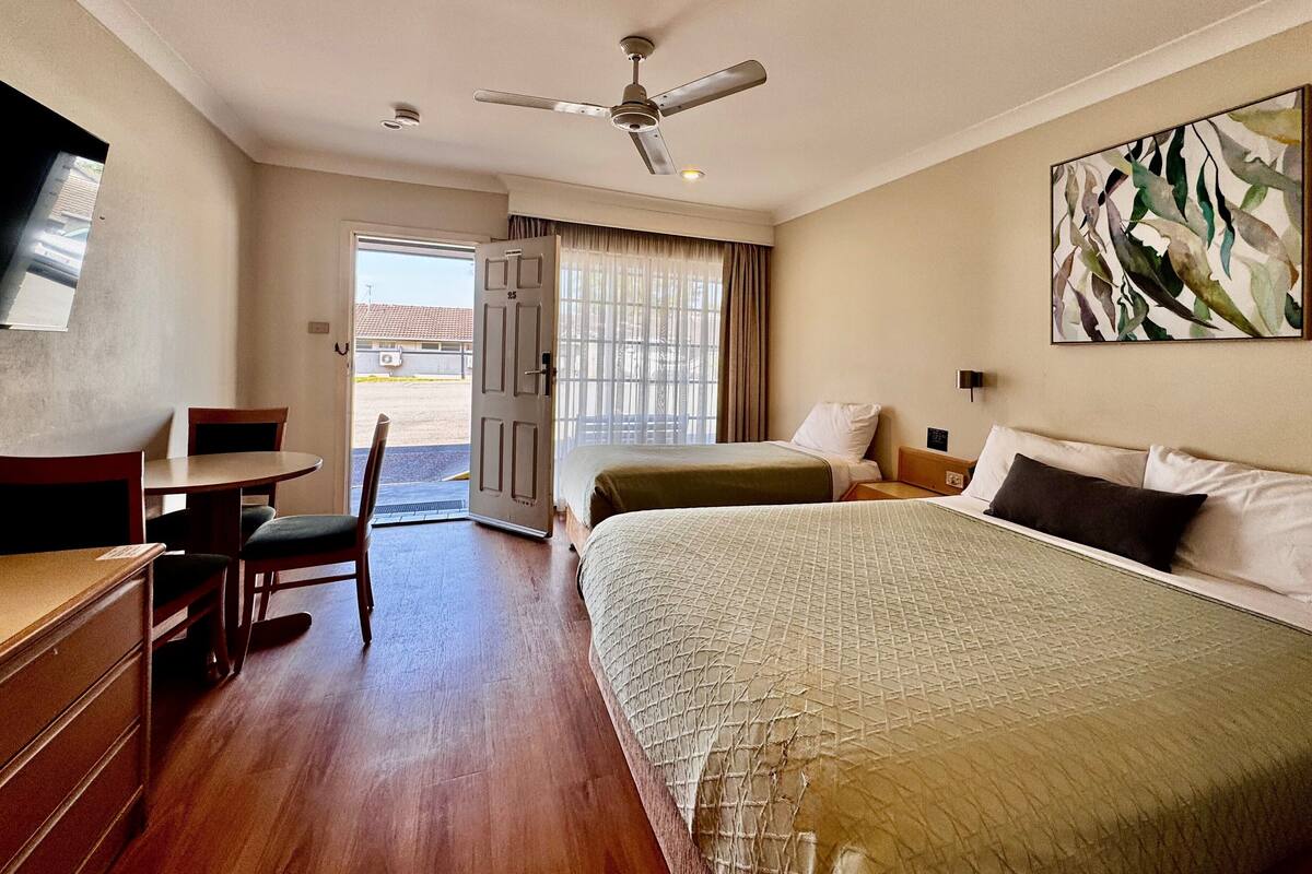 A hotel room with a bed, a desk, a chair, a ceiling fan, and a door leading to a balcony.