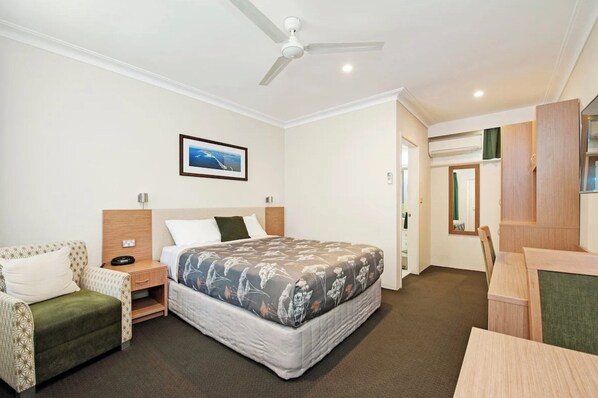 A hotel room with a bed, a desk, a chair, a ceiling fan, and a framed picture on the wall.