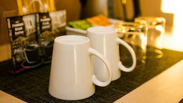 Two white mugs on a table with a placemat, a coffee maker, and a glass of water in the background.
