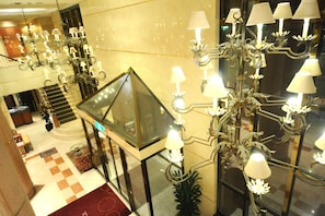 Um hall de entrada com várias luminárias de cristal, um elevador de vidro e piso xadrez.