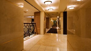 Een hotelgang met een marmeren vloer, een leuning en een lange, smalle trap die uitkomt op een plateau.