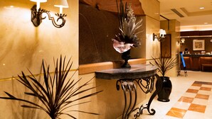 Een lobby met een receptiebalie, een decoratieve wand met een groot bloemarrangement en een geruit vloerpatroon.