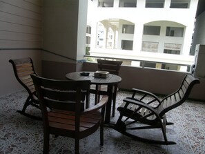 A balcony with a table and chairs, a tiled floor, and a view of a building with multiple balconies. - Anchana House by Zuzu (Pattaya)