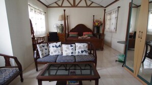 A room with a sofa, a bed, a wooden table, and a fan. - Anchana House by Zuzu (Pattaya)